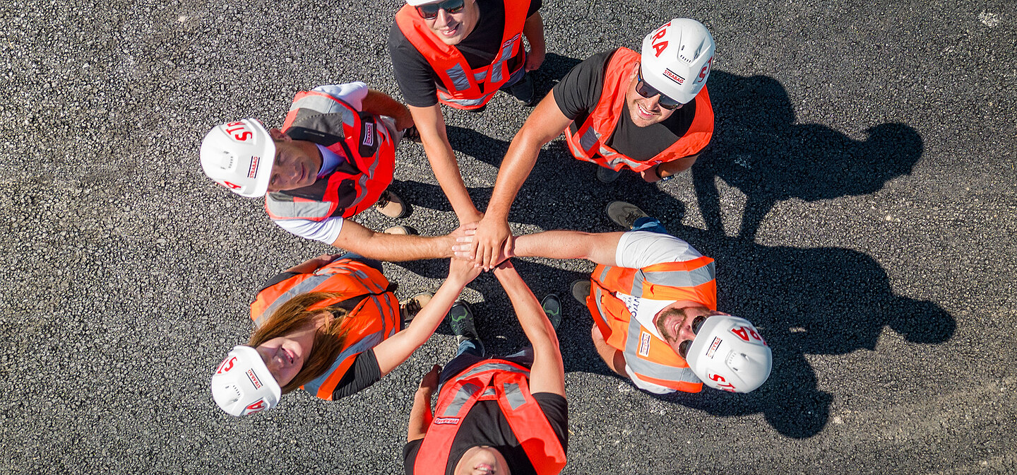 Picture of 6 people from a bird's eye view standing in a circle with their hands in the middle