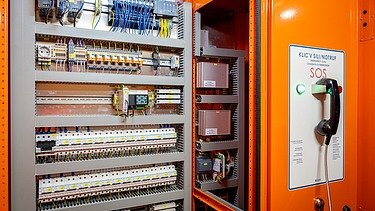 The picture shows an emergency call pillar and an open switch cabinet