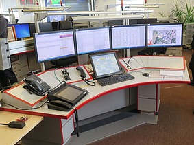 Image of a control center desk with screens and operating devices