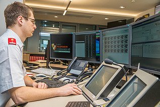 Das Bild zeigt einen Dispatcher, Bildschirme und Systeme auf einem Leitstellentisch