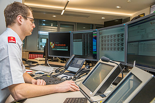 The picture shows a dispatcher, screens, and systems on a control center desk.