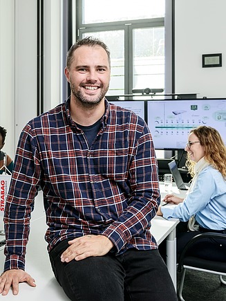Picture of a smiling man half-sitting on a desk