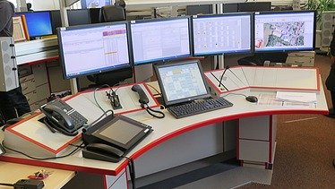 Bild eines Leitstellentisches mit Bildschirmen und Bediengeräten