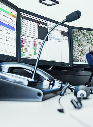 Das Bild zeigt einen Leitstellentisch mit Bildschirmen und Dispatcher