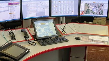 Bild eines Leitstellentisches mit Bildschirmen und Bediengeräten
